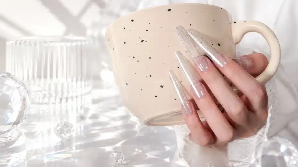 A manicured hand holding a ceramic cup, demonstrating the zero background color and glass-like transparency of JTING Platinum Crystal Cat Eye gel.