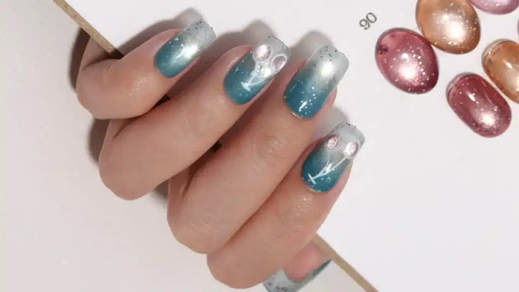 Raw mobile phone camera capture of a hand display featuring ocean blue gradient cat eye nails and delicate hand painted cherry art