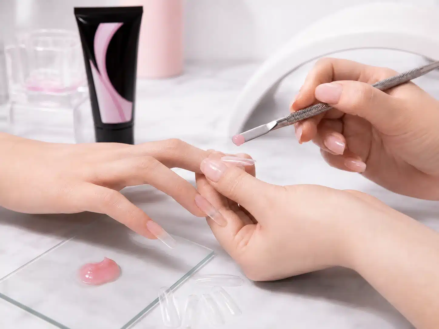 Professional nail technician shaping poly gel on a dual form with a spatula during a poly gel nail extension application