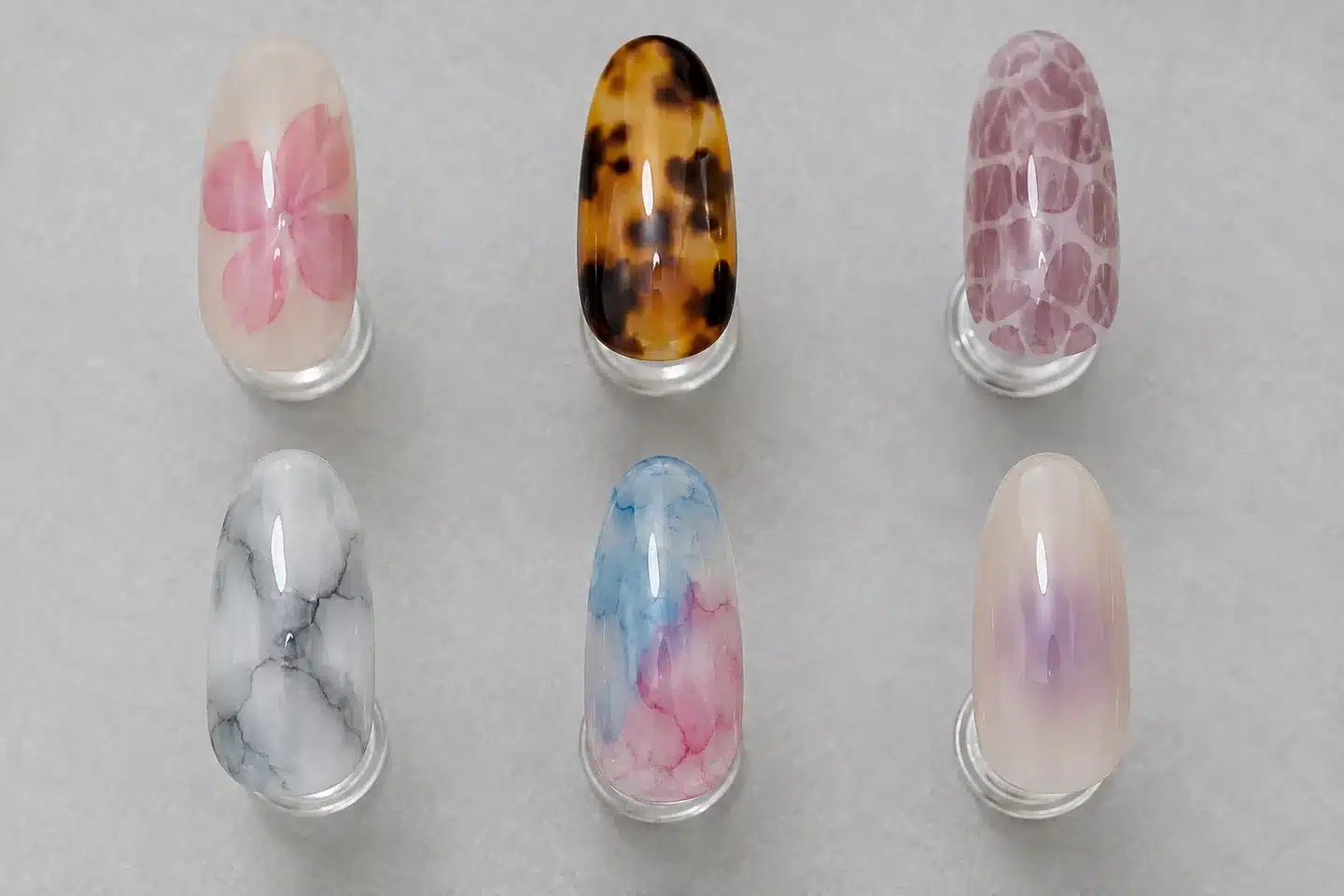 Six nail art design concepts showing pink flowers, tortoiseshell, reptile pattern, gray marble, watercolor and a lavender halo