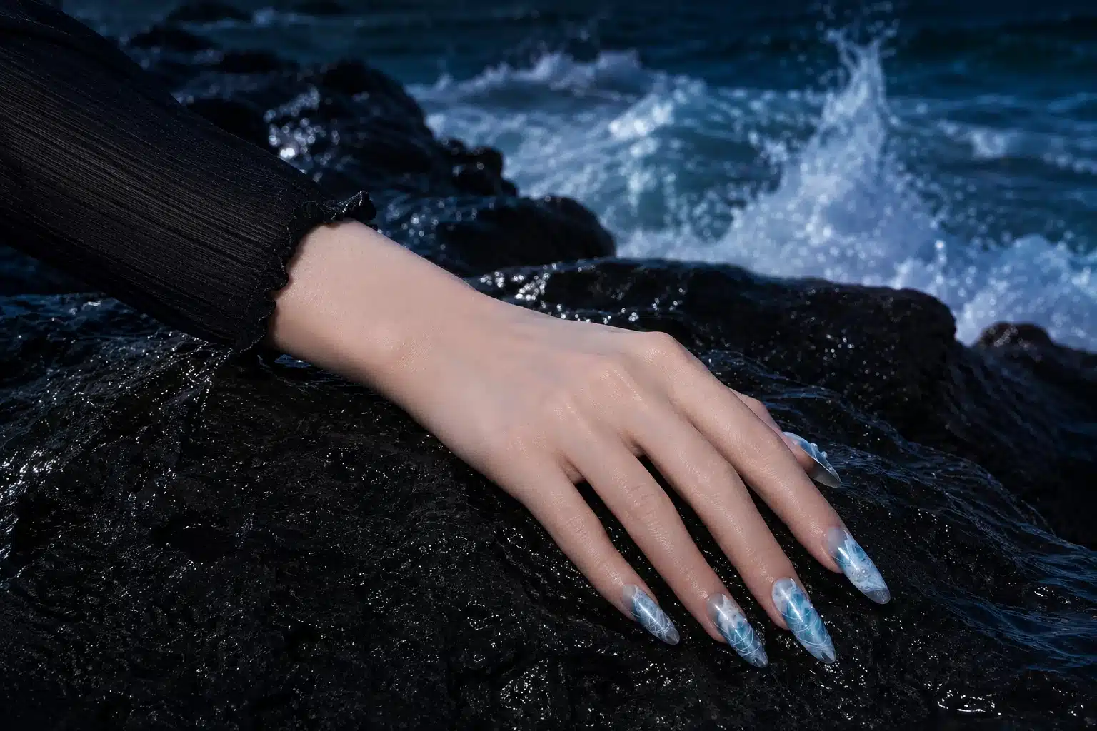 Blue, teal and silver Sea Wave Gel nail art worn on a hand resting on wet coastal rock with ocean waves behind