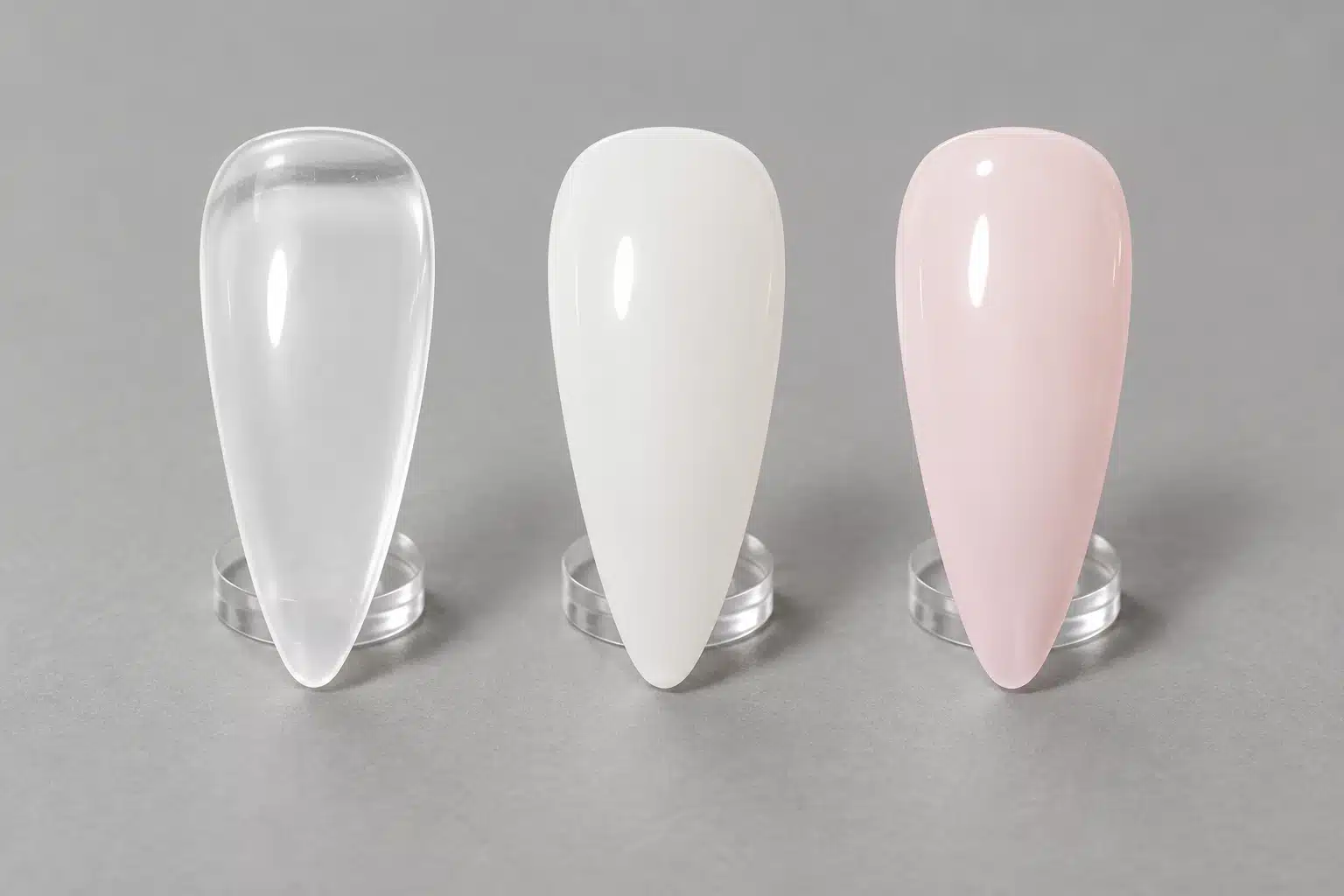 Clear, milky white and pale pink nail swatches displayed side by side on transparent stands.