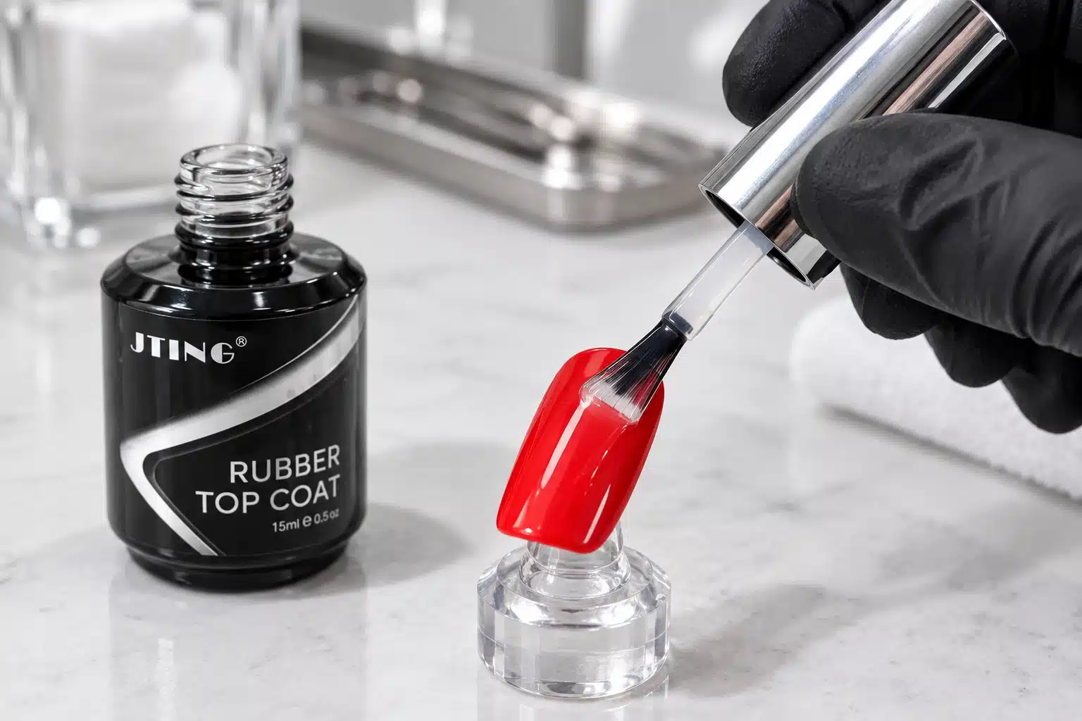 Thin clear top coat application on a red nail tip beside JTING Rubber Top Coat