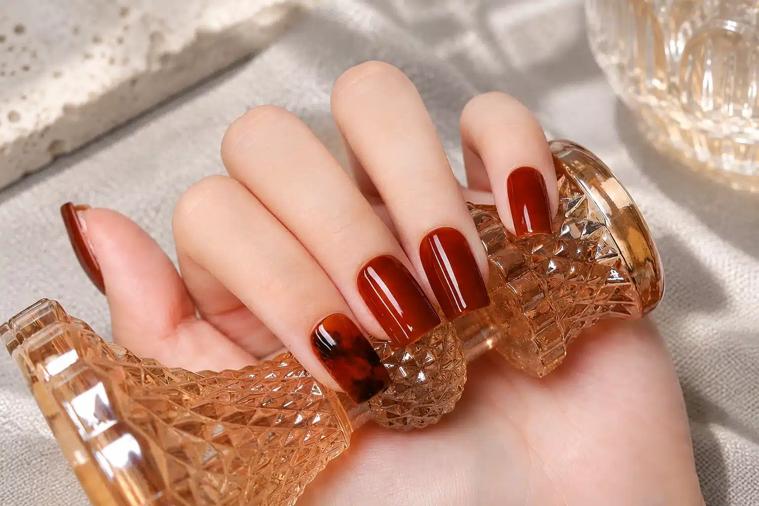 Short square amber jelly nails with a tortoiseshell accent, shown holding a faceted amber glass object.