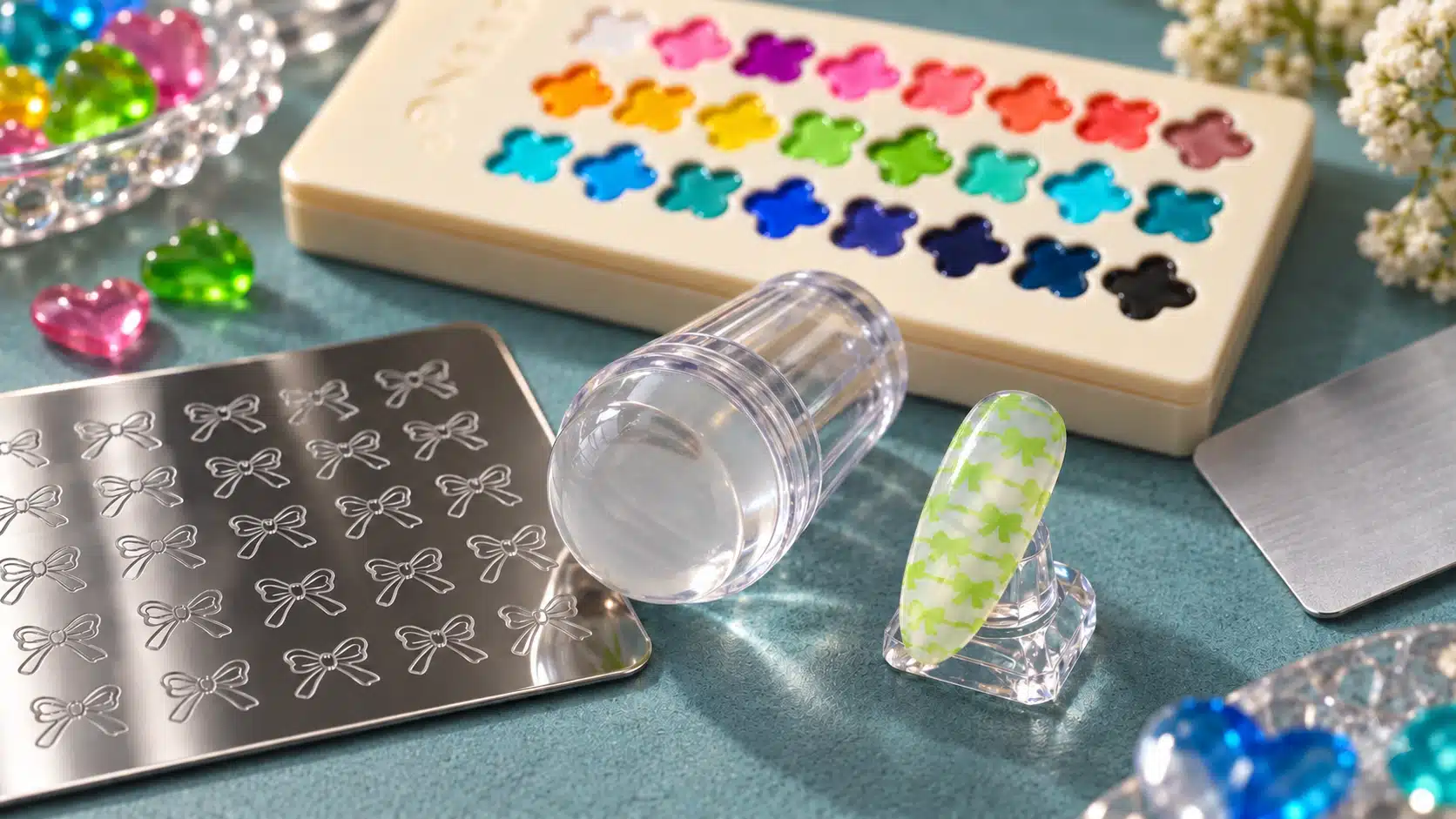 Green bow-pattern nail tip beside a metal stamping plate, clear stamper and JTING clover palette