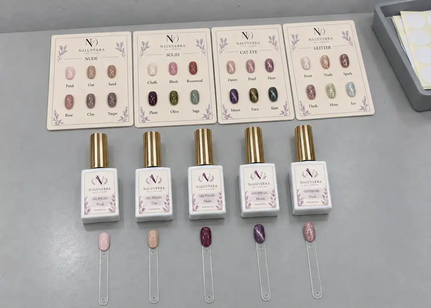 Nude, solid, cat-eye and glitter gel polish samples arranged on a supplier’s gray workbench for seasonal shade selection