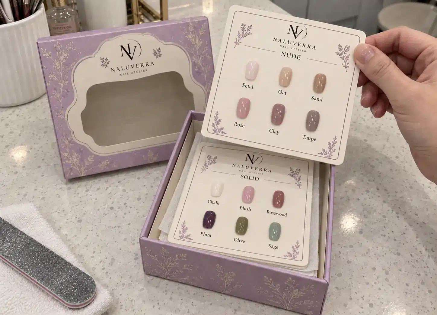 A hand lifting a matte shade card from the original lilac storage box