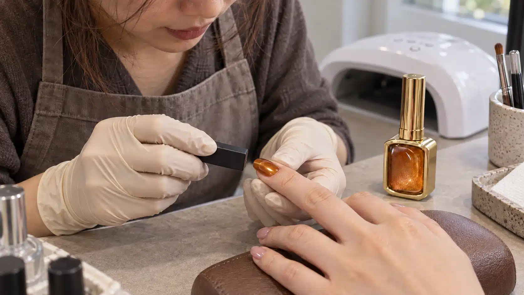 Nail technician holding a magnet beside an amber cat-eye nail, with the gold gel bottle on the workbench