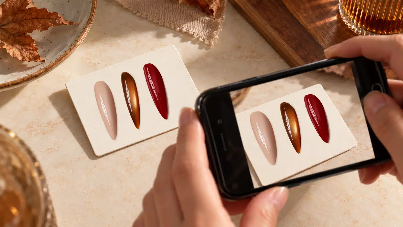 Hands using a smartphone to photograph autumn nail samples on a cream display card