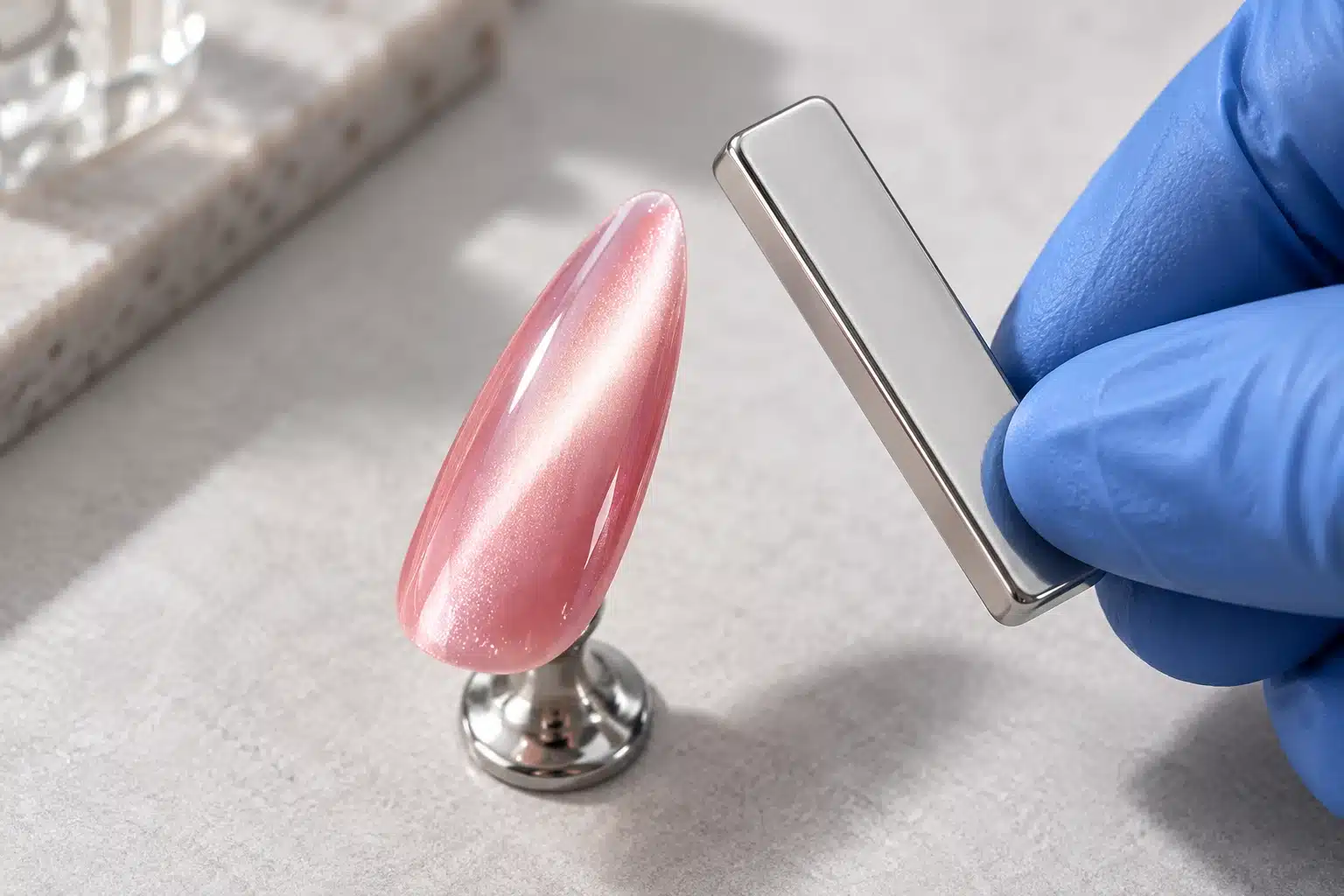 Gloved hand holding a silver bar magnet beside a pink water-light nail tip without touching it