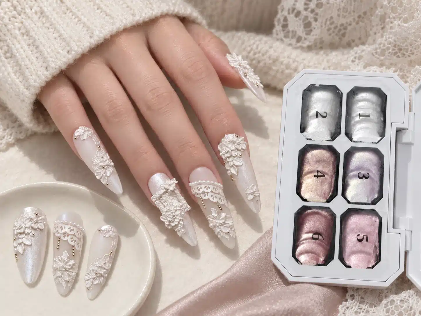 Hand model wearing white floral and lace relief nails beside the Dusty Pink Sculpture Gel six-color palette and sample tips