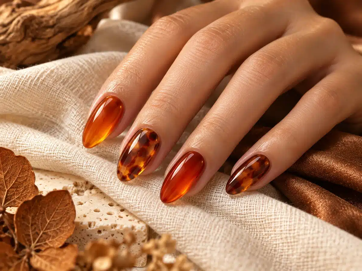 Glossy amber and tortoiseshell-inspired gel nail art on a hand resting on ivory linen