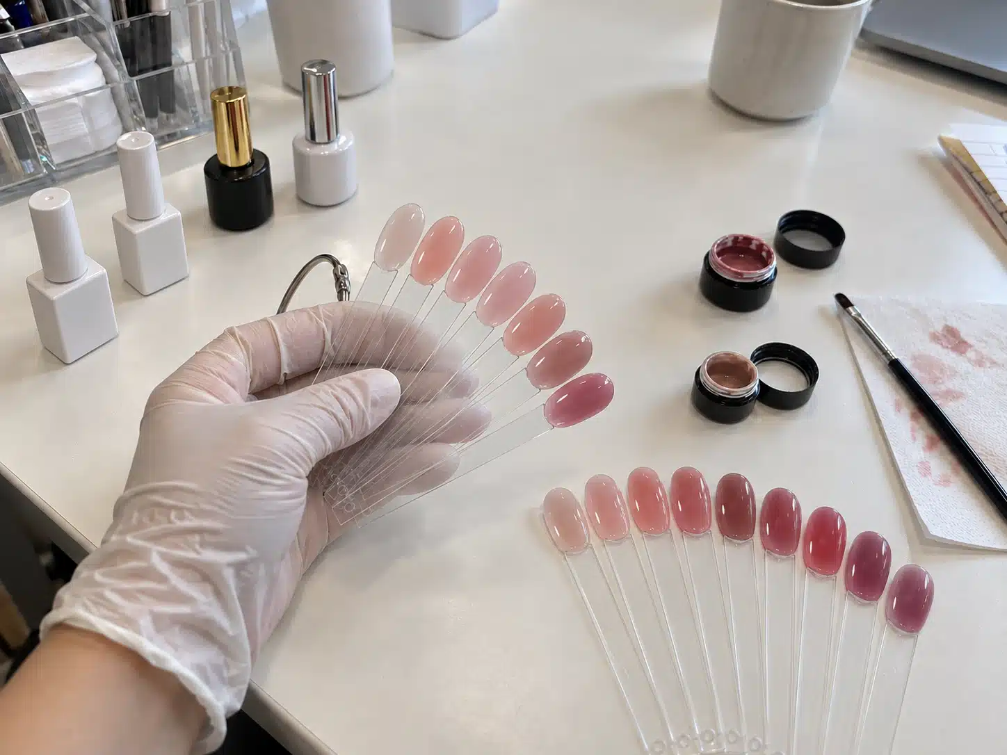 Comparing nude and pink gel nail polish shades on clear swatch sticks