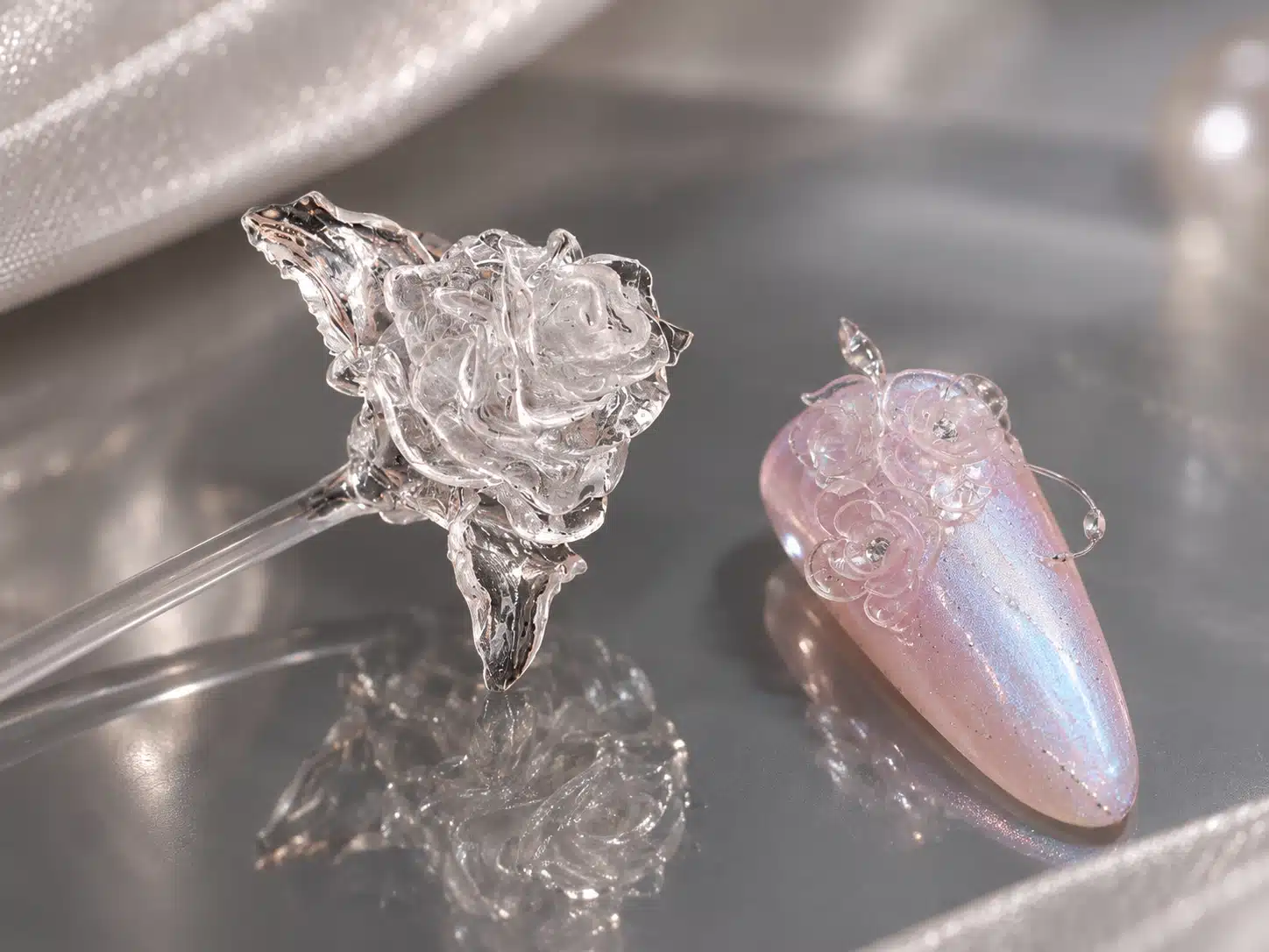 Clear sculpted rose on a display stick beside transparent rose details on a pink iridescent nail