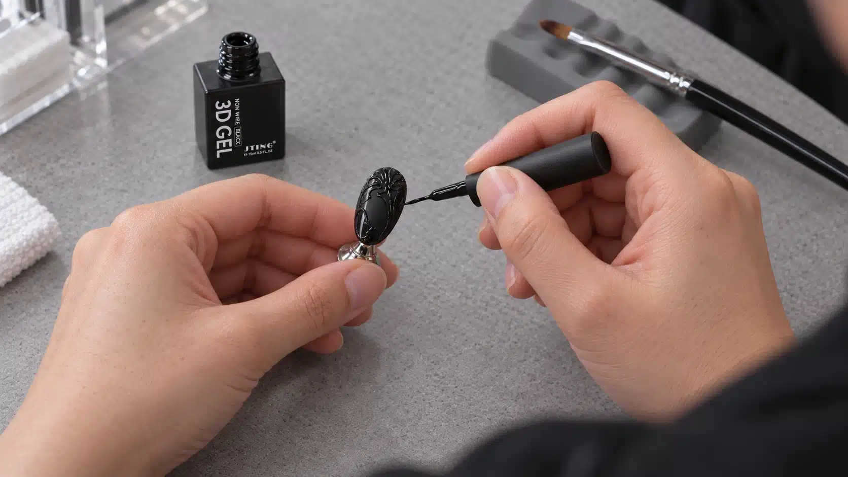 Technician drawing raised black floral lines with the bottle brush beside a separate sculpting brush