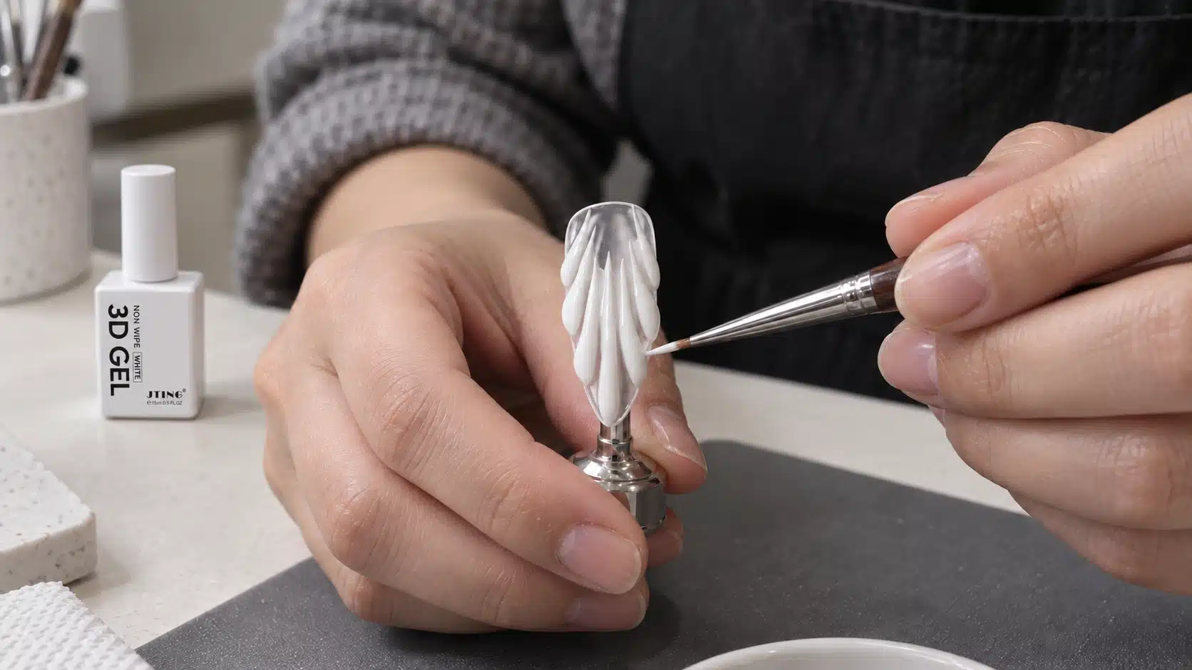 Nail technician refining a white relief petal on a mounted nail tip with a sculpting brush