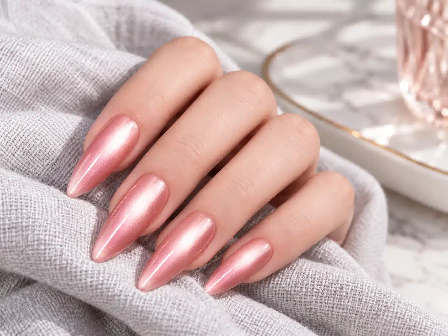 Long pink water-light cat eye nails with broad luminous bands resting on gray fabric
