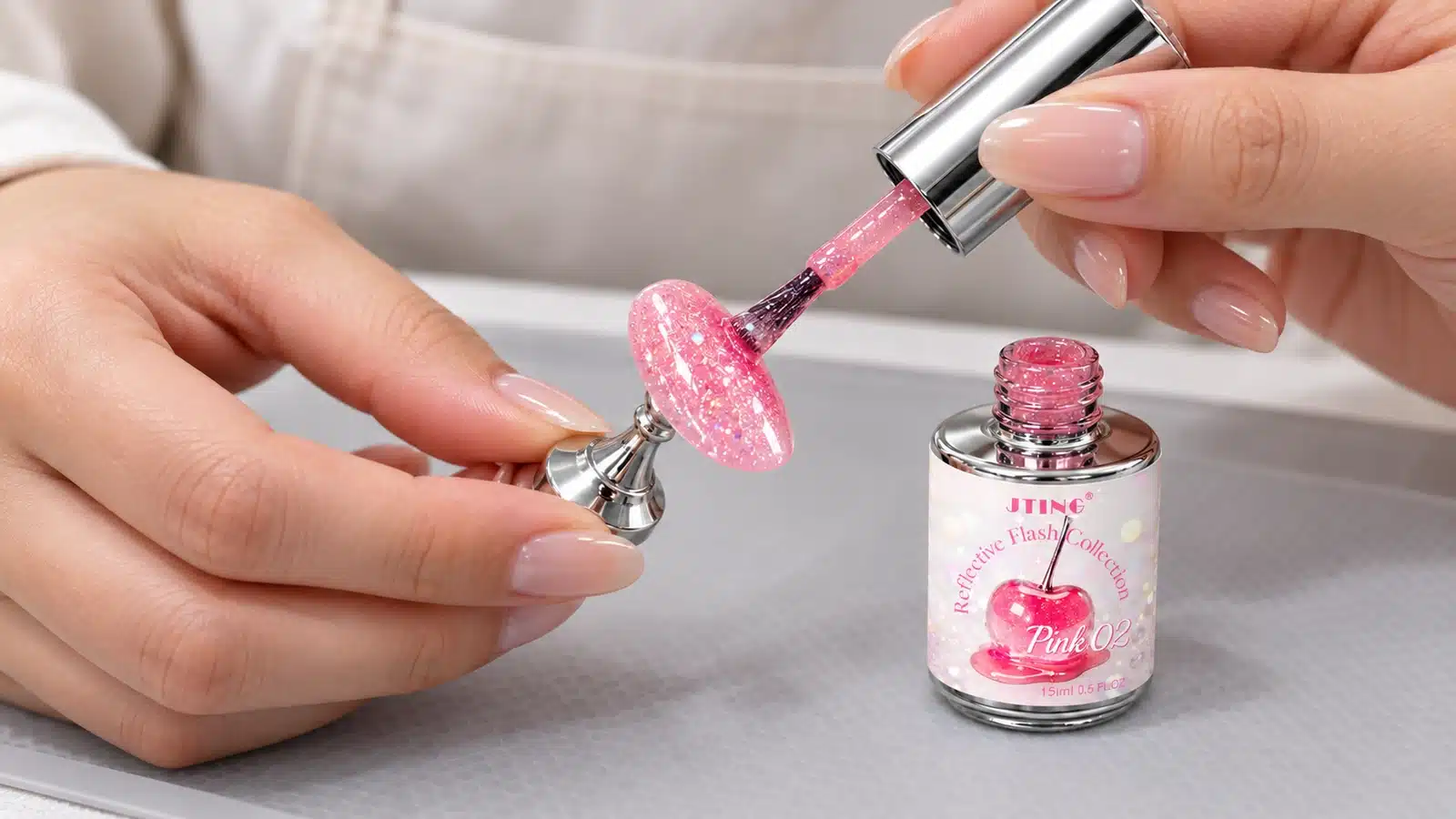 Technician brushing pink reflective gel onto a nail tip held on a small display stand