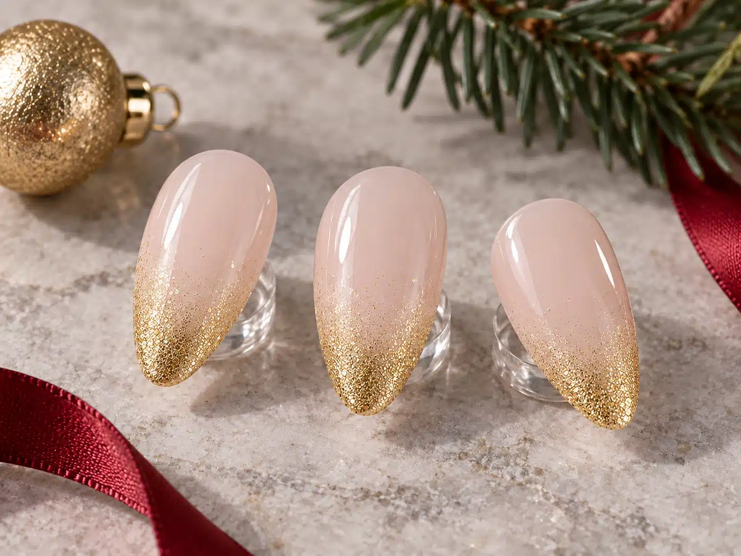 Almond blush nail samples with fine gold glitter fading from the tips toward a clear foundation