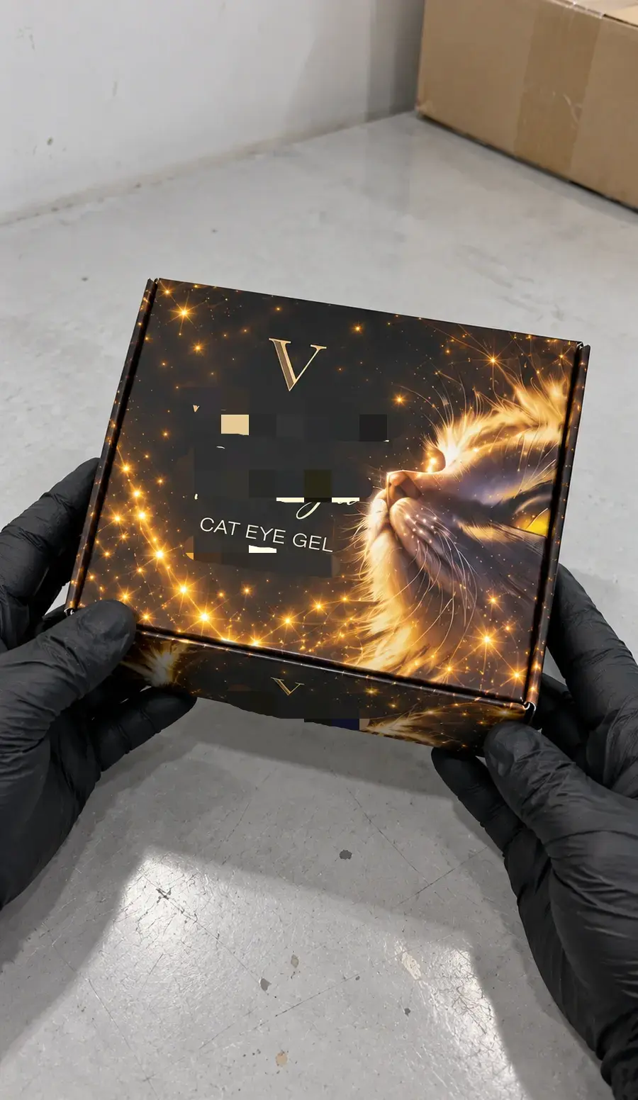 Gloved hands holding a closed VYRELUNE Gold Light cat eye gel collection box above a factory worktable.