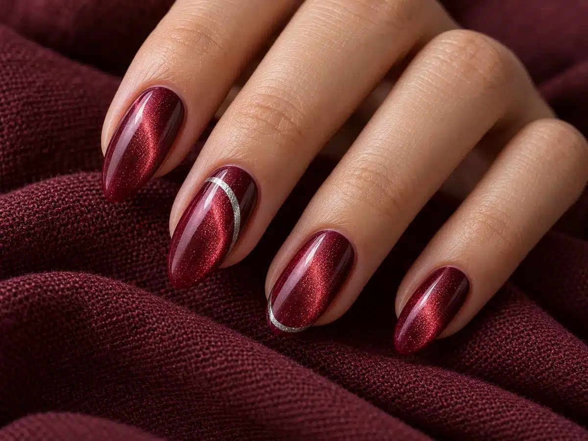 Burgundy almond cat eye manicure with fine silver curves and a silver French accent